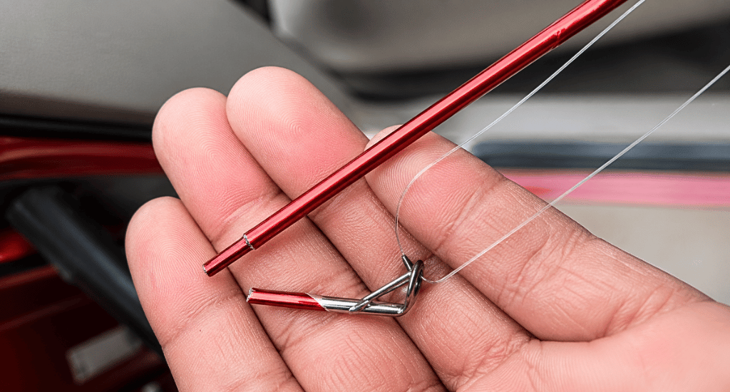 A person's hand holds a broken red fishing rod. The tip is snapped off, with the fishing line still threaded through the silver guide on the detached piece.