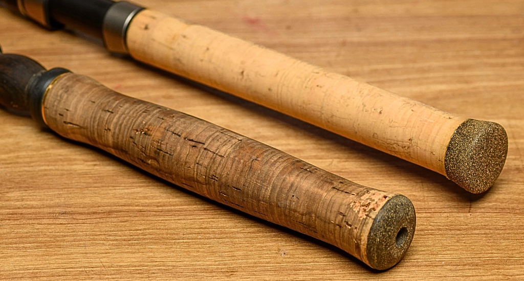 Close-up of two fishing rod cork handles on a wood surface. One handle is weathered and dark brown, while the other is newer, light tan, and has a rounded end cap.