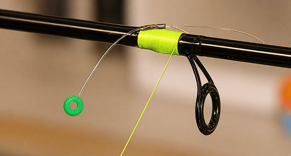 Close-up of a fishing rod with a lime green strike indicator bead attached via a clear loop. It’s secured with matching neon tape near a black ceramic guide.