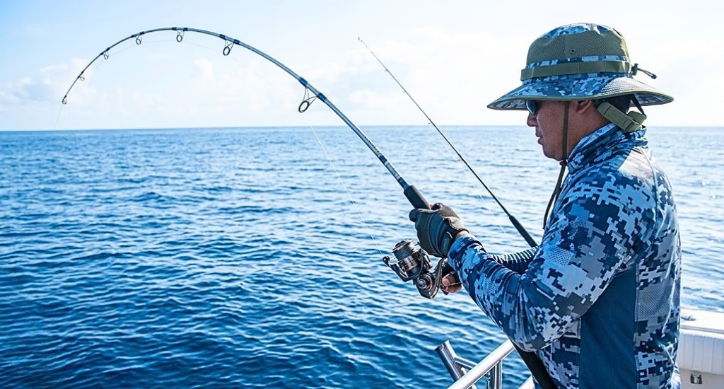 An angler in protective clothing holding a deeply bent fishing rod while ocean fishing from a boat.