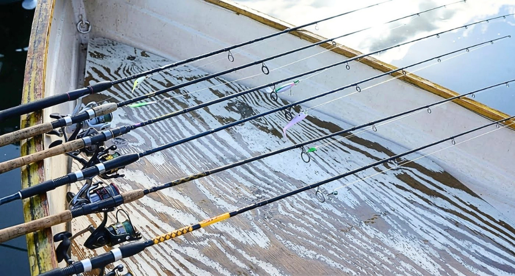 Multiple spinning and casting fishing rods with reels lined up side-by-side inside a wooden boat.