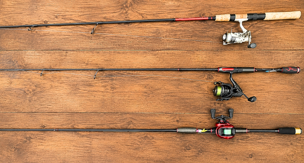 Three various fishing rods with reels, including spinning and baitcasting setups, laid out on a wooden surface.