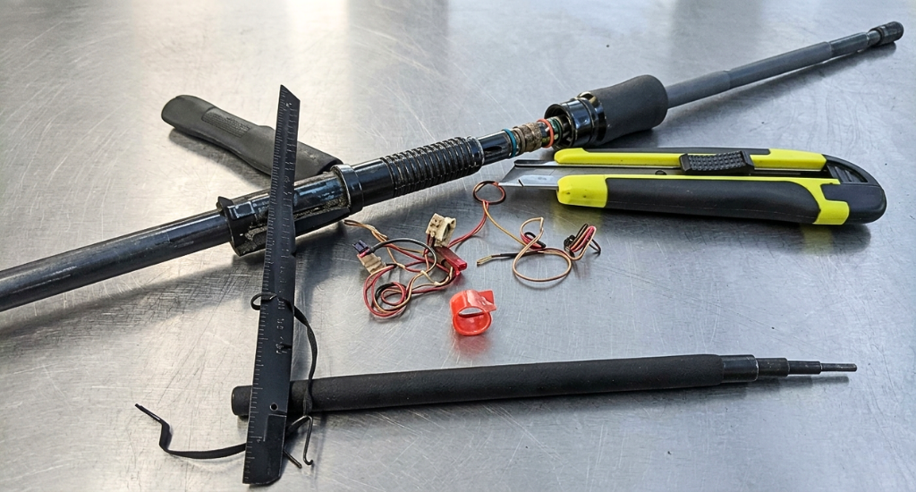 A disassembled black fishing rod with electronic wires and tools on a metal surface.