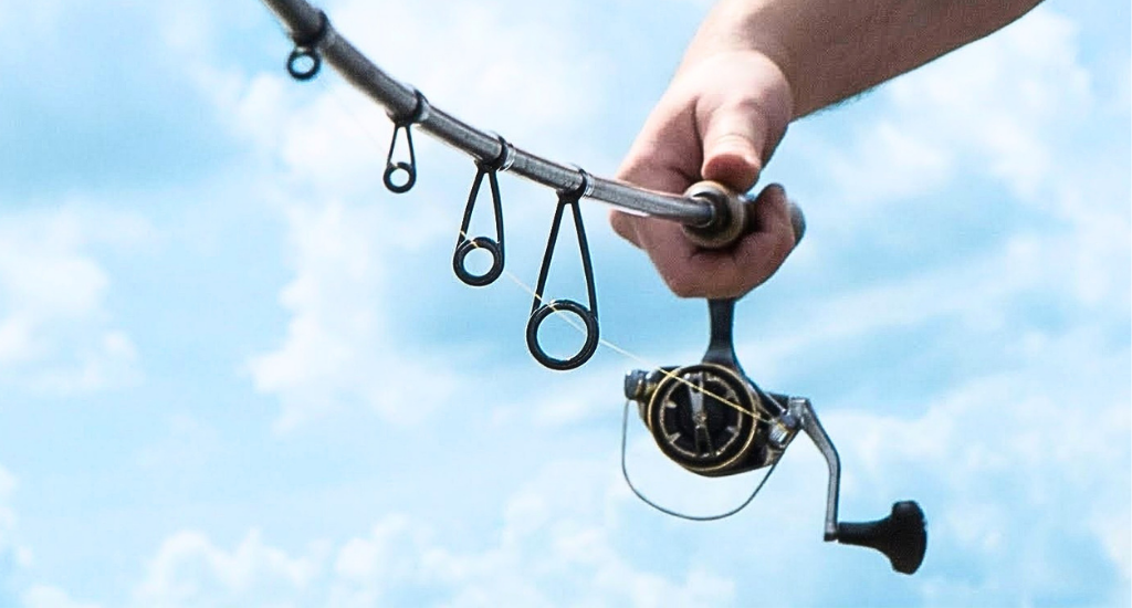 A hand holding a spinning rod upside down against a cloudy sky, showing a row of line guides decreasing in size.