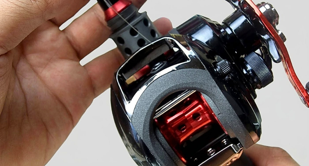 A close-up of an angler threading fishing line through the line guide of a black and red baitcasting reel.
