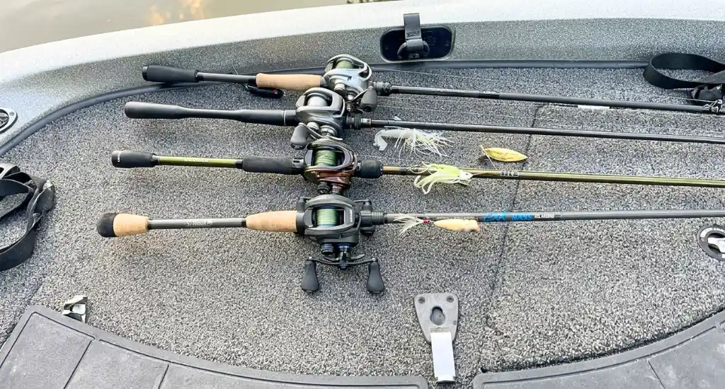 Four rigged baitcasting rods with lures attached lying in a row on the deck of a bass boat.