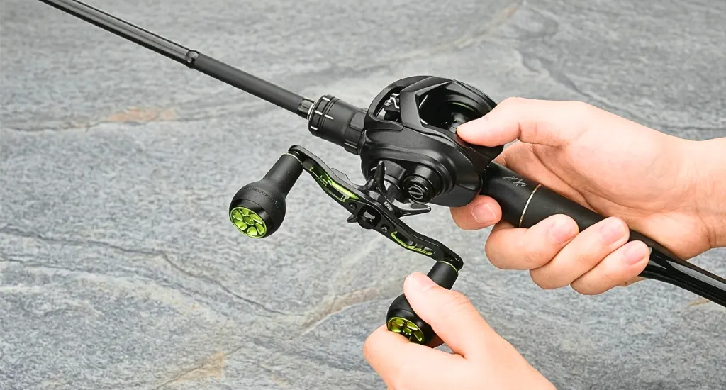 Hands holding a black baitcasting reel attached to a fishing rod on a gray stone surface.