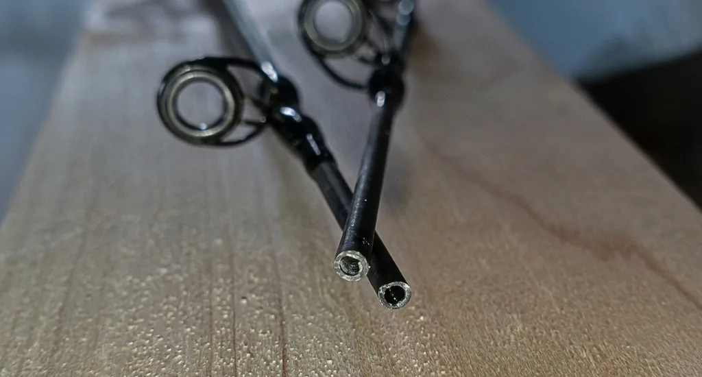 Close-up view of hollow carbon fiber fishing rod blank ends resting on a wooden surface showing the break point.