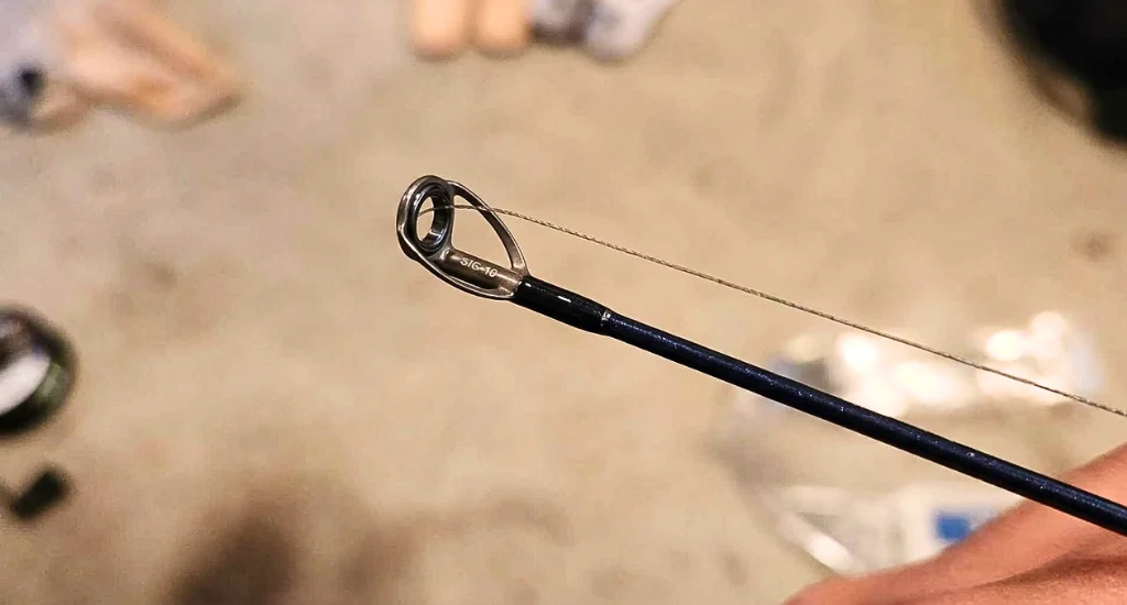Close-up view of a newly installed metal tip top on a dark blue fishing rod blank with braided line threaded through.