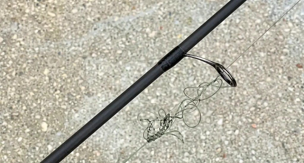 Tangled green monofilament fishing line bunched up below a line guide on a black rod blank.